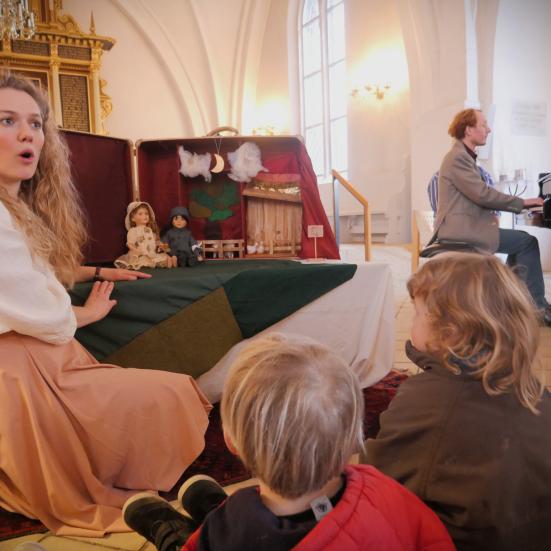 Anne Wæhrens spiller dukketeater for rn gruppe børn og pianist Kristoffer Kaad spille ibaggrunden på et flygel.