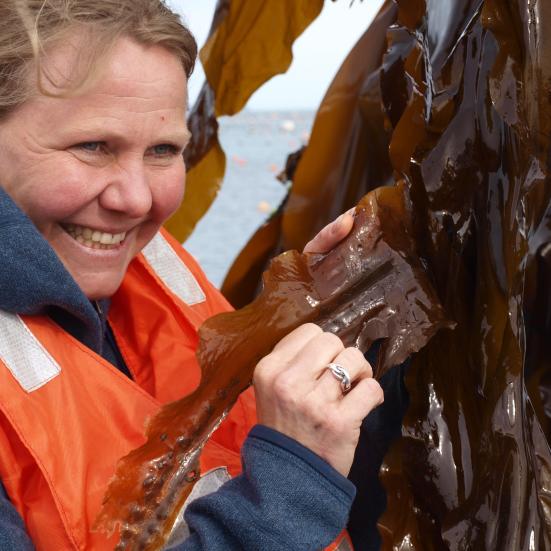 Foredragsholder Anette Brun i redningsvest ser på noget tang.