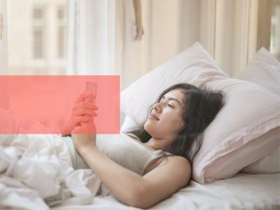 Ung kvinde ligger i seng og læser på sin telefon